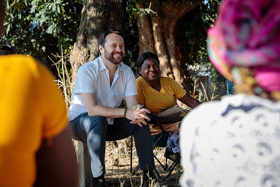 Jason Carter sits under a tree with women in Zambia.
