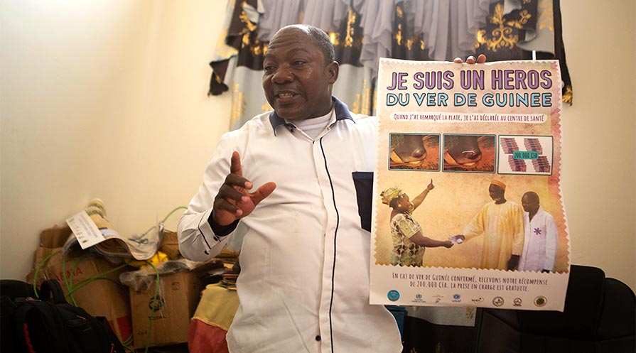 Dr. Moussa Saye displays a Carter Center poster that announces rewards for Malian citizens who report Guinea worm cases.