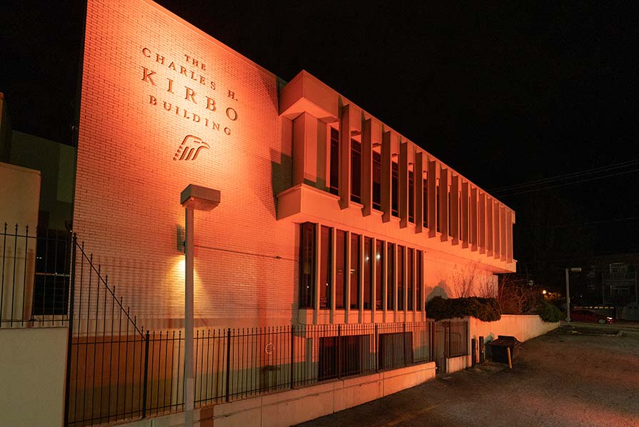 Photo of the front exterior of the Carter Center's Kirbo building illuminated with orange light.