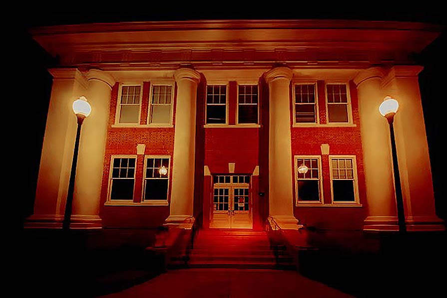 Photo of the front exterior of Plains High School illuminated with orange light.