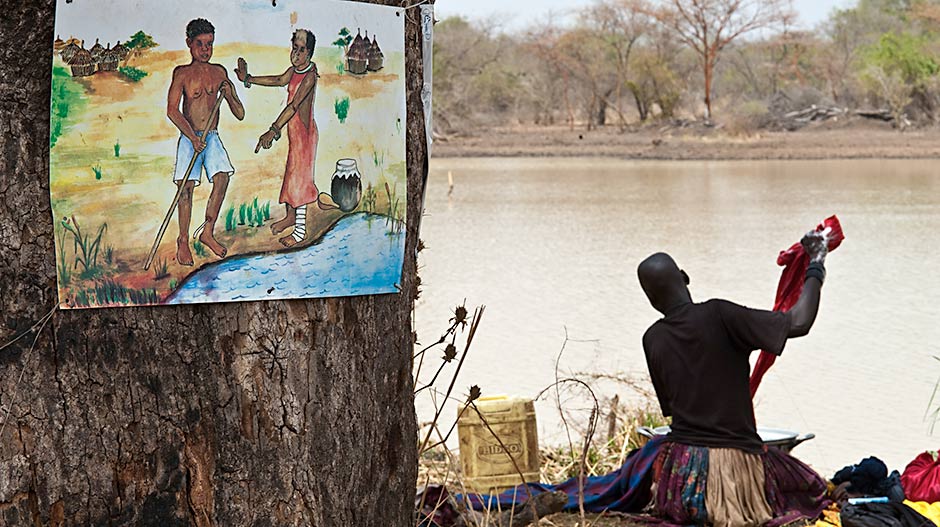 A woman does her washing at a roadside dam in Terkeka County, South Sudan, next to a sign warning that a person with an emerging Guinea worm should not enter the water due to the danger of spreading the water-borne parasitic disease. The temptation to enter water is great because of the burning sensation caused by an emerging worm. (Photo: The Carter Center/L. Gubb)