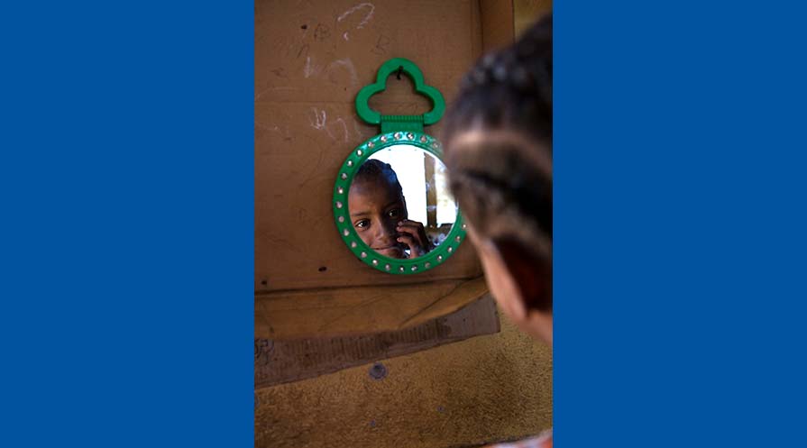 Photo of a young girls reflection in a green hand mirror that hangs on a wall.