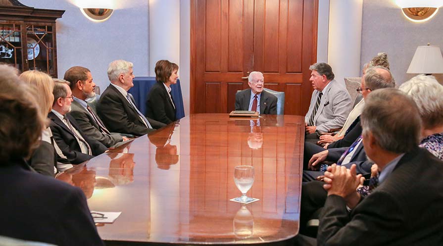 Photo of President Carter sitting at the head of a boardroom table with board members.