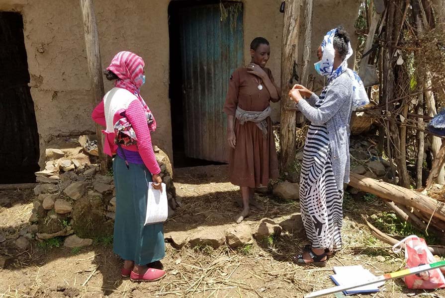 Photo of two health workers talking to a woman in a village in Ethiopia.