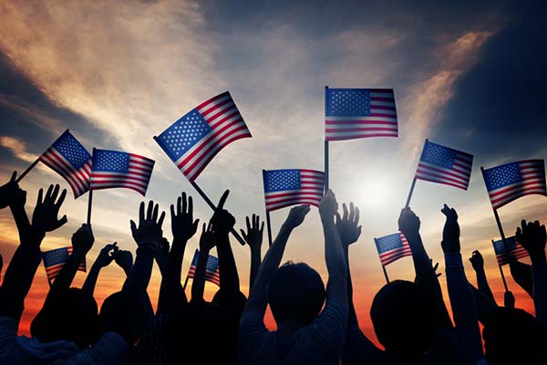 Hands waving the American flag against a dusk sky.